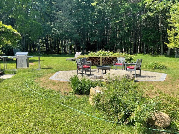 A patio area with a grill, outdoor furniture, and a fire pit surrounded by greenery.