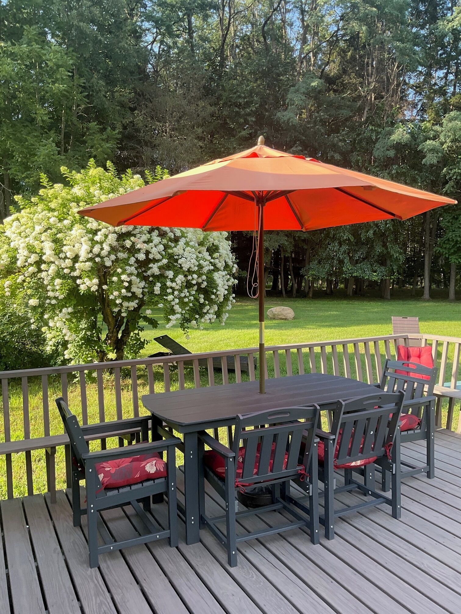 Eine Terrasse mit Tisch und Stühlen, einem Sonnenschirm sowie ein Garten mit Bäumen und Blumen.