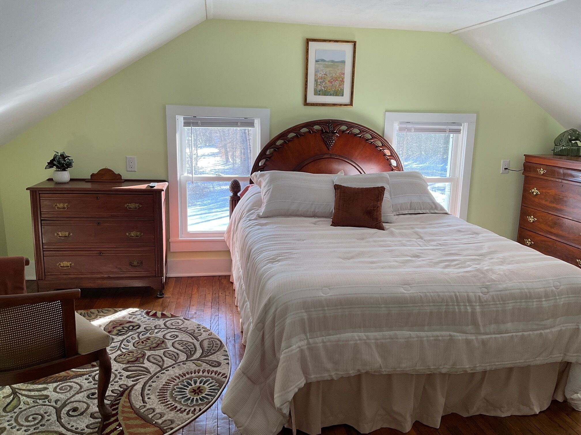A bedroom with a large bed, wooden dresser, and two windows.