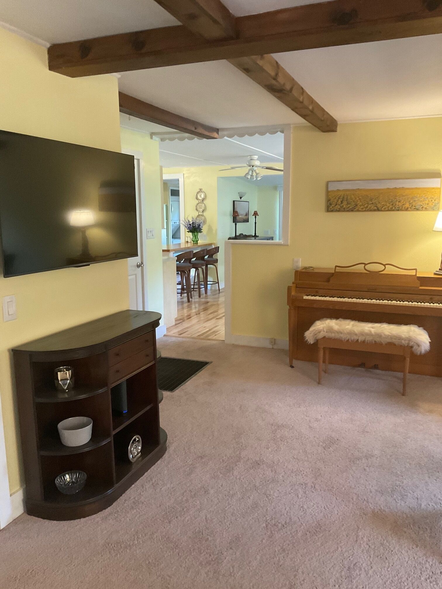 Una sala de estar con televisor de pantalla plana, un mueble de madera oscura para entretenimiento, un piano y un comedor al fondo.