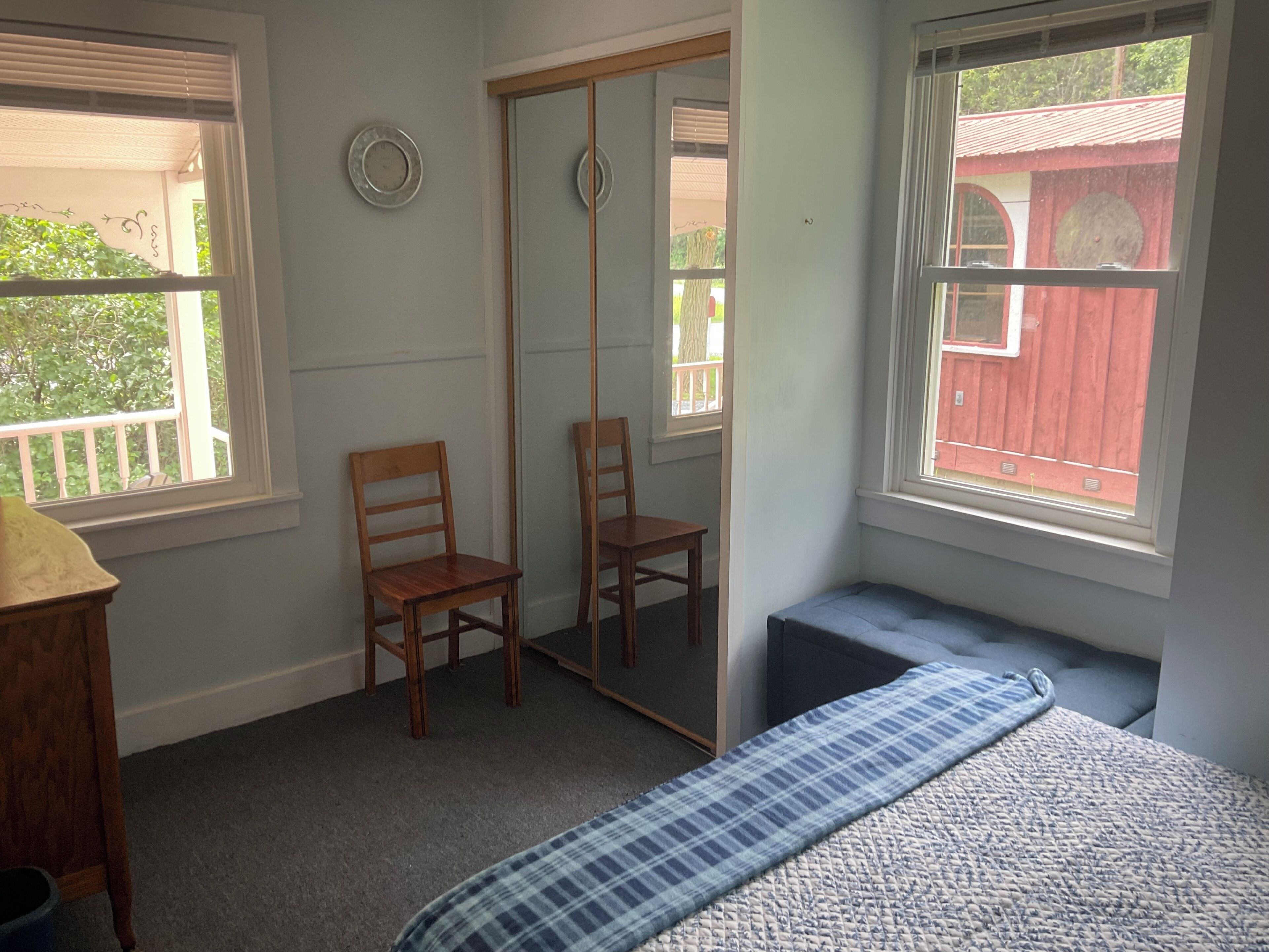 Un dormitorio con una cama, dos sillas, un espejo y ventanas.