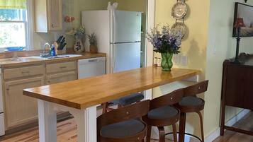 A kitchen with a wooden table and bar stools, a refrigerator, and a vase with flowers on the counter.