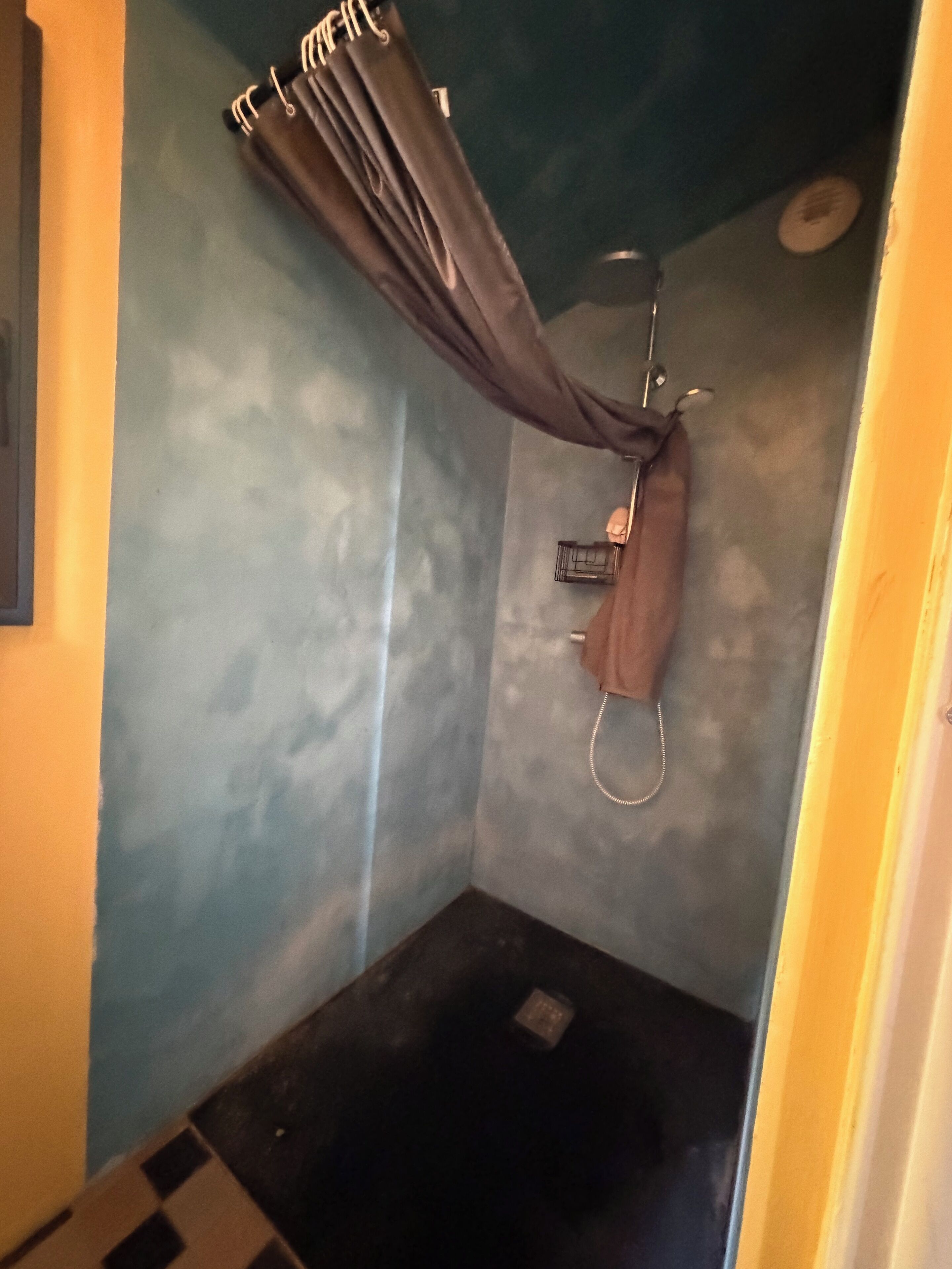 Een kleine, afgesloten douchecabine met een douchegordijn, een handdouche en een kraan op de muur.