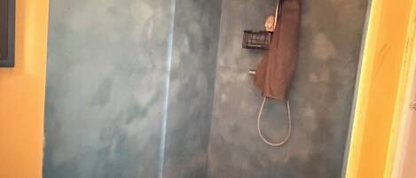 Um chuveiro pequeno e fechado, com cortina, chuveiro manual e torneira fixada na parede.