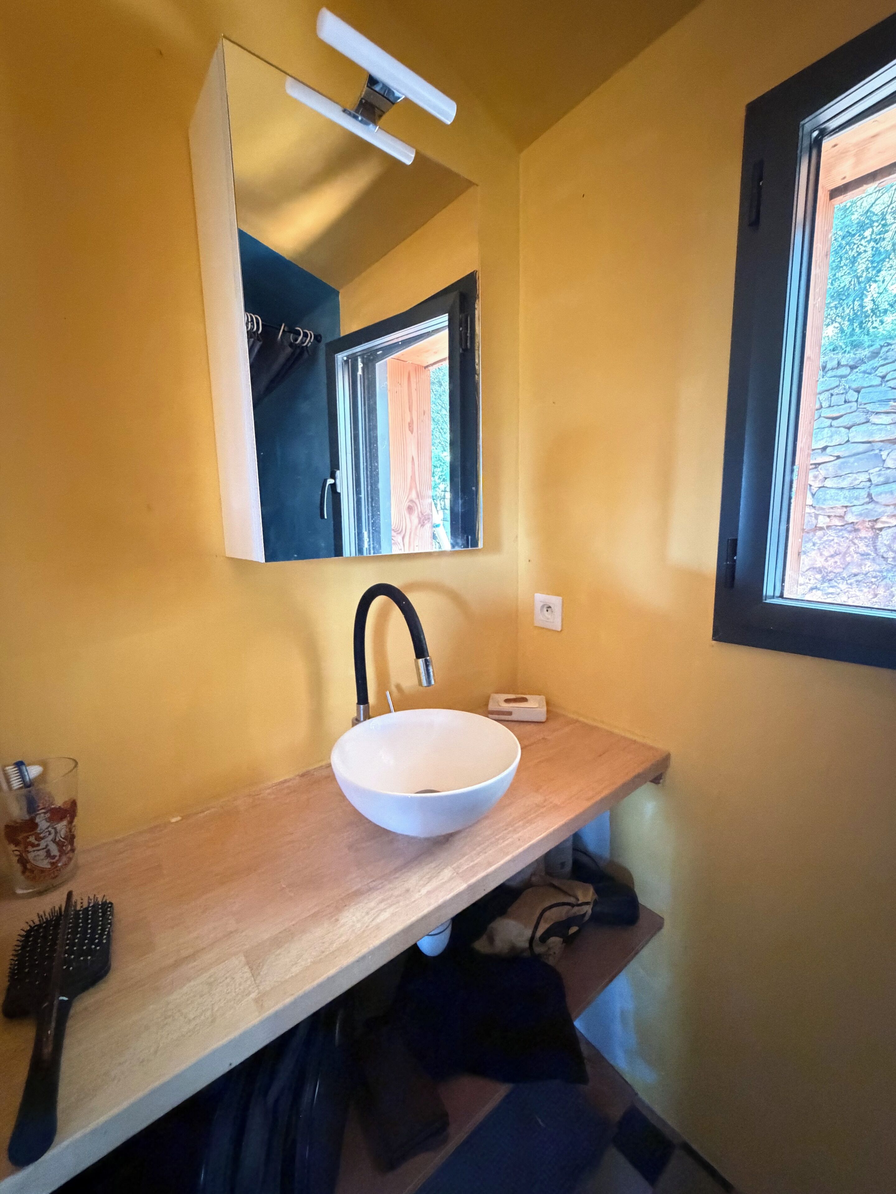 Une salle de bain avec un lavabo blanc, un miroir et une fenêtre.