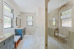 Un bagno moderno con cabina doccia in vetro, una panca e uno specchio grande.