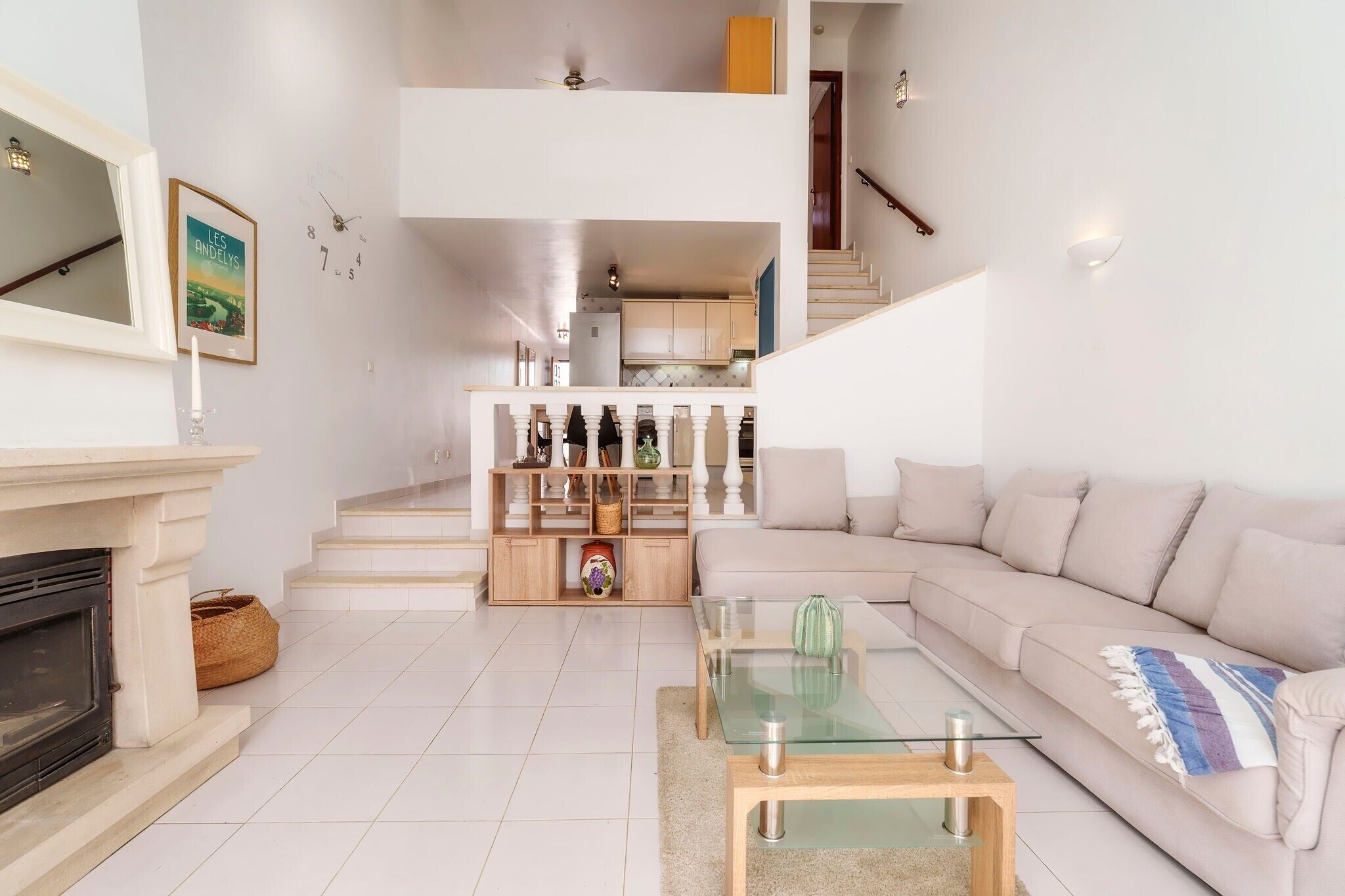 Un salon moderne avec une cheminée, une table basse en verre, un canapé beige et une cuisine en arrière-plan.