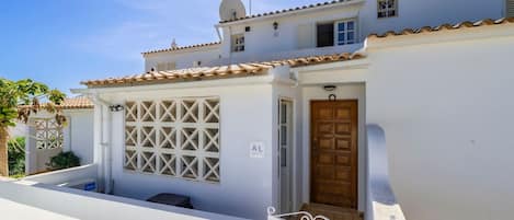 Um edifício branco com telhado de azulejos, porta de madeira e portão branco.