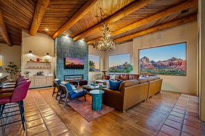 A spacious living area with a fireplace, large windows with mountain views, and a wooden ceiling. - Vortex/Red Rock View/Sauna/Pool/ HotTub/Dome/Games (Sedona)