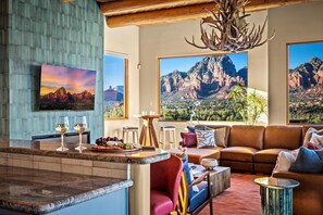 A modern living room with a large window, a fireplace, and a dining area with a bar. - Vortex/Red Rock View/Sauna/Pool/ HotTub/Dome/Games (Sedona)