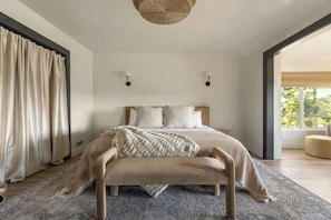 A bedroom with a bed, bedside lamps, a bench, and a large window. - Two Birds - expansive lake views and walk to lake (Lake Arrowhead)