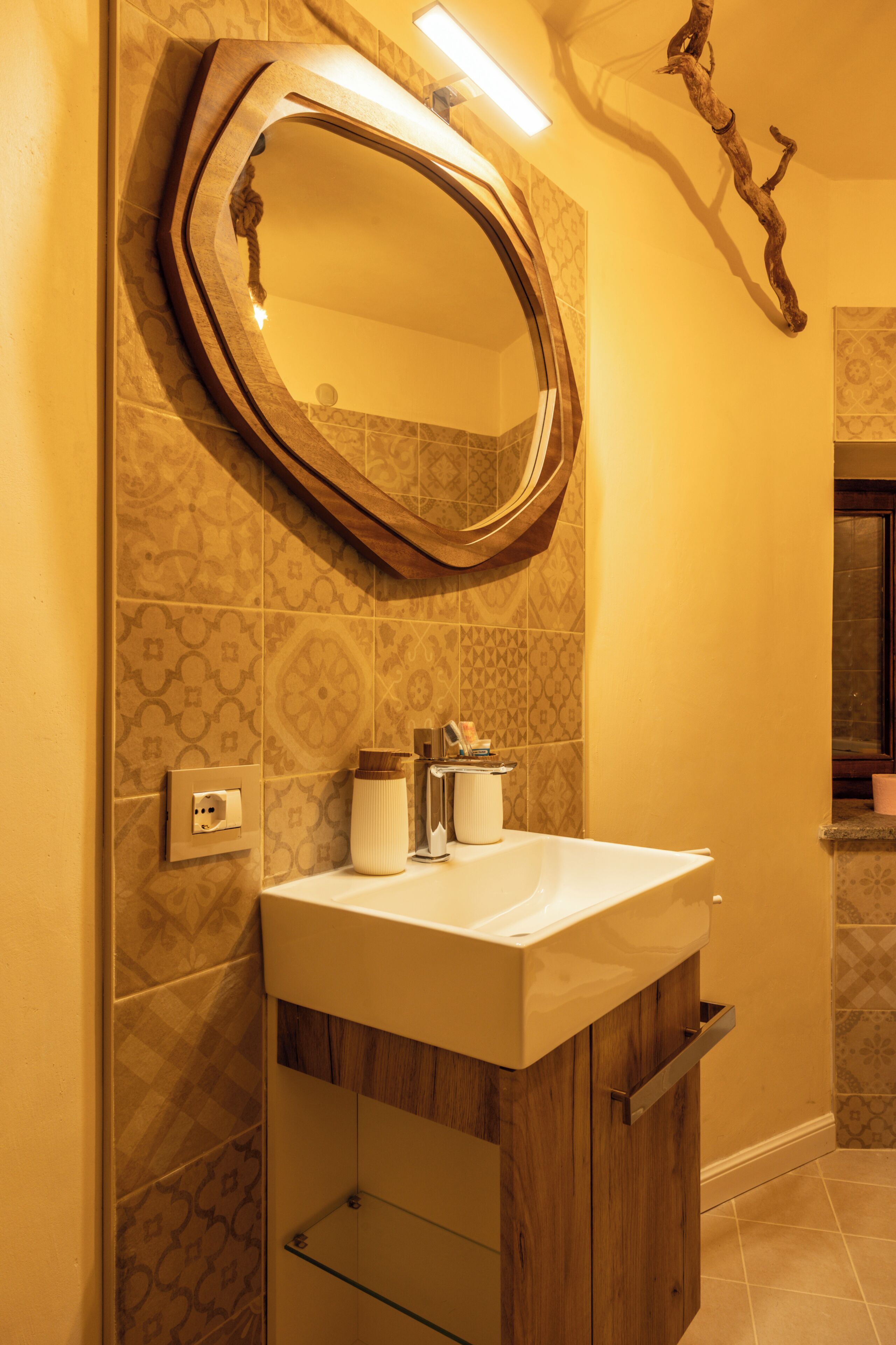 Une salle de bain dotée d’un grand miroir ovale, d’un lavabo blanc, de meubles en bois et de carreaux muraux à motifs.