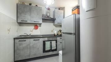 Eine Küche mit grauen Schränken, einem Edelstahlkühlschrank, einem eingebauten Backofen und einer Pendelleuchte.