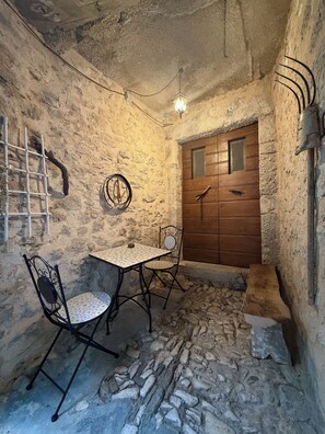A stone-walled room with a wooden door, a metal-framed table with a chair, and a hanging light fixture. - Casetta nel Borgo (Caso)