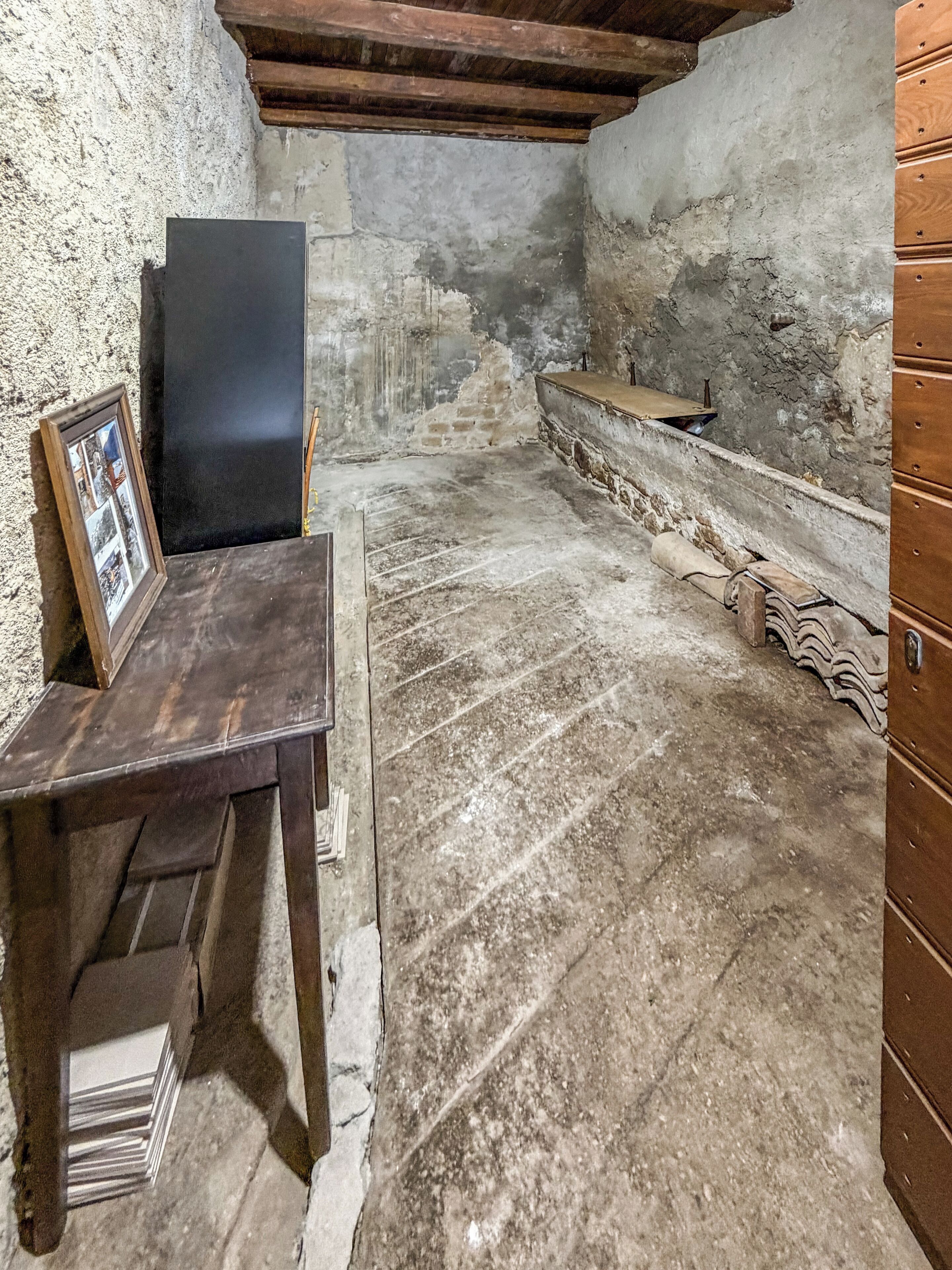 Una habitación con una mesa de madera, un cuadro enmarco, un panel oscuro y un banco de piedra.