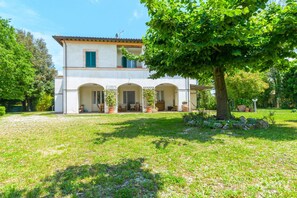 Une maison à deux étages avec un porche couvert, une pelouse et un grand arbre.