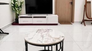 Una sala de estar moderna con una mesa de centro de mármol, un televisor de pantalla plana sobre un mueble blanco y una puerta de madera.