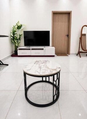 A modern living room with a marble coffee table, a flat-screen TV on a white cabinet, and a wooden door.