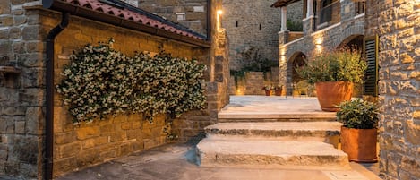 A stone courtyard with steps leading to a building, potted plants, and a wall with climbing plants.