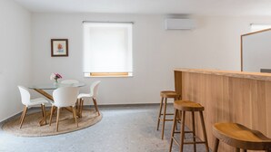 A room with a round glass table, white chairs, a wooden bar, and a large window. - Platano, ADQ (Buje)