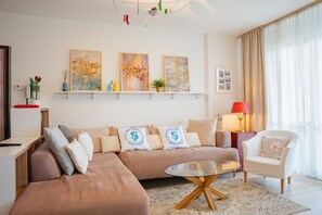 Ein modernes Wohnzimmer mit einer Couch, einem Glastisch und einem Sessel. An Wandschränken befinden sich dekorative Gegenstände und Kunstwerke.
