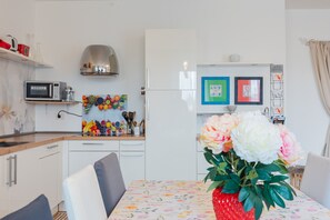 Eine moderne Küche mit weißen Schränken, einer Mikrowelle und einer Obstschale. Es gibt einen Esstisch mit Stühlen und eine Vase mit Blumen.