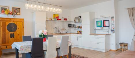 A modern kitchen with white cabinets, a dining area with a table and chairs, and a chandelier.