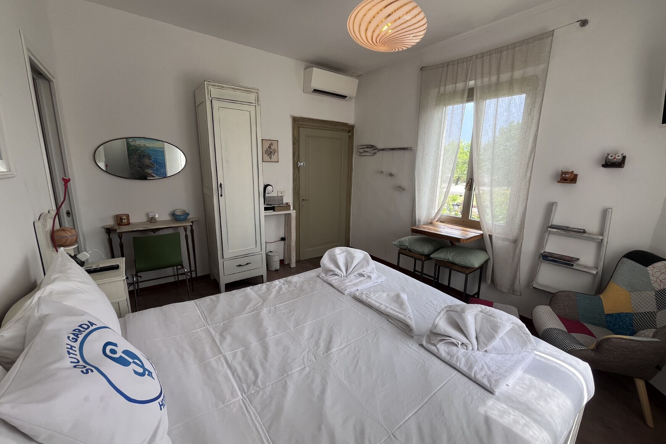 A hotel room with a bed, a desk, a chair, a wardrobe, a mirror, and a window with curtains.