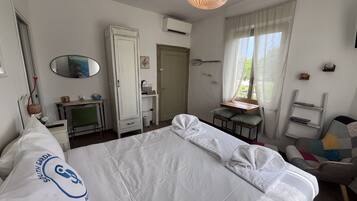A hotel room with a bed, a desk, a chair, a wardrobe, a mirror, and a window with curtains.