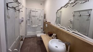 A bathroom with a shower, toilet, sink, and a large mirror.