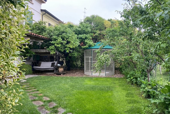 A garden with a green lawn, a wooden bench, a covered seating area, and a greenhouse.