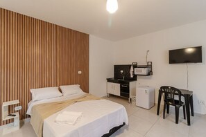 Quarto de hotel com cama, escrivaninha, televisão, micro-ondas e pequeno frigorífico.
