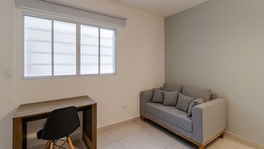 A room with a sofa, a desk, and a window with blinds. - Studio 12 com Wi-fi e Pr Ximo ao Shopping Tatuap (São Paulo)