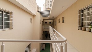 A narrow corridor with a white railing, potted plants, and a staircase leading to an upper level. - Studio 12 com Wi-fi e Pr Ximo ao Shopping Tatuap (São Paulo)