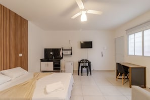 Quarto com cama, escrivaninha, cadeira, televisão e ventoinha no teto.