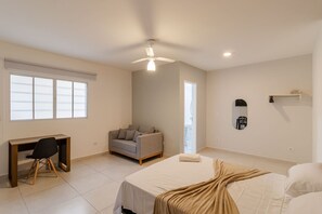 Quarto com cama, escrivaninha, cadeira, sofá, ventoinha no teto e janela.