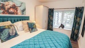 A bedroom with a large bed, a headboard, a window with curtains, and a painting on the wall. - Hidden Gem (Windermere)