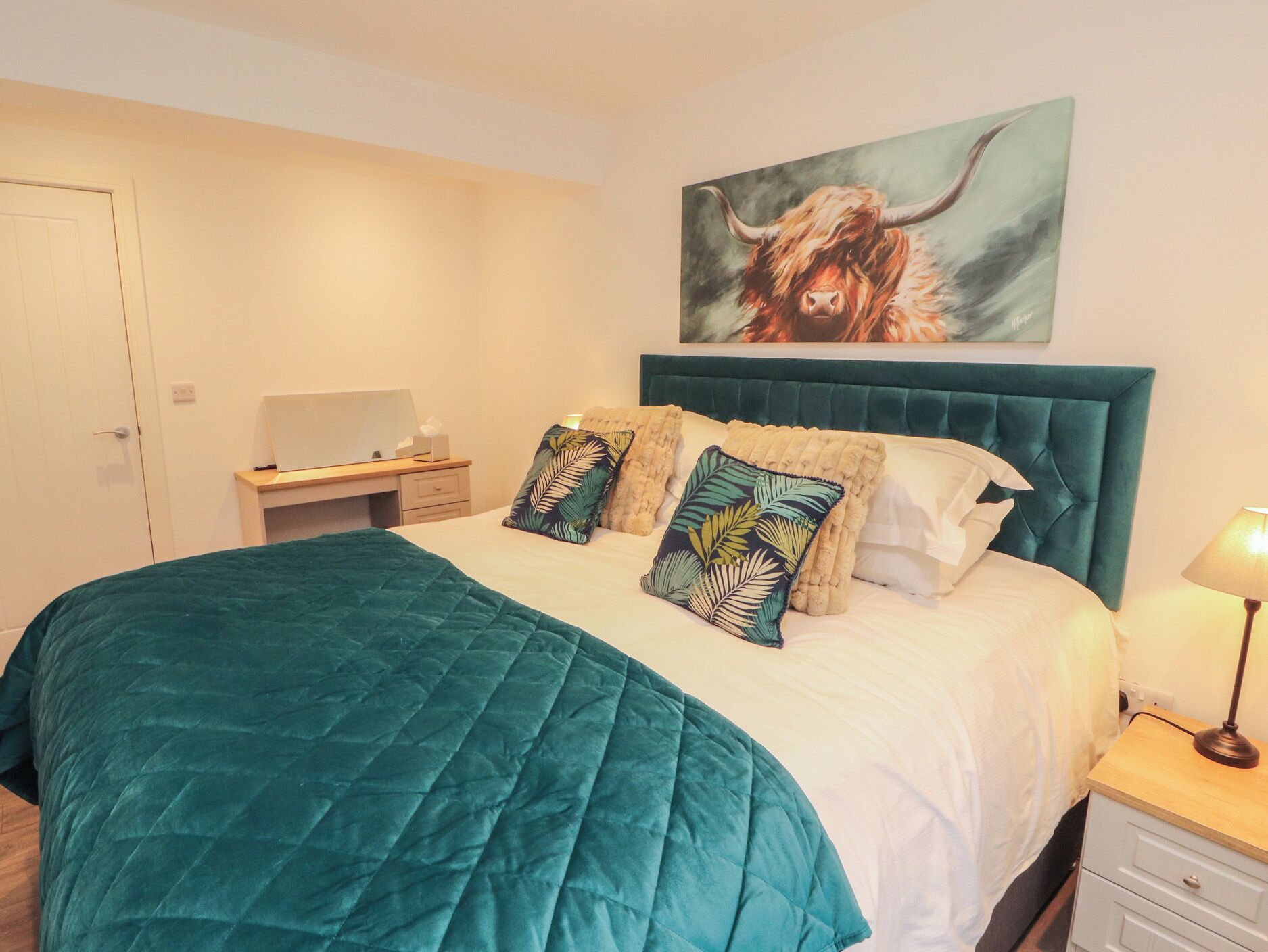A bedroom with a bed, a desk, a chair, a lamp, and a painting on the wall.