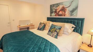 A bedroom with a bed, a desk, a chair, a lamp, and a painting on the wall.