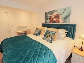 Un dormitorio con cama, escritorio, silla, lámpara y un cuadro en la pared.