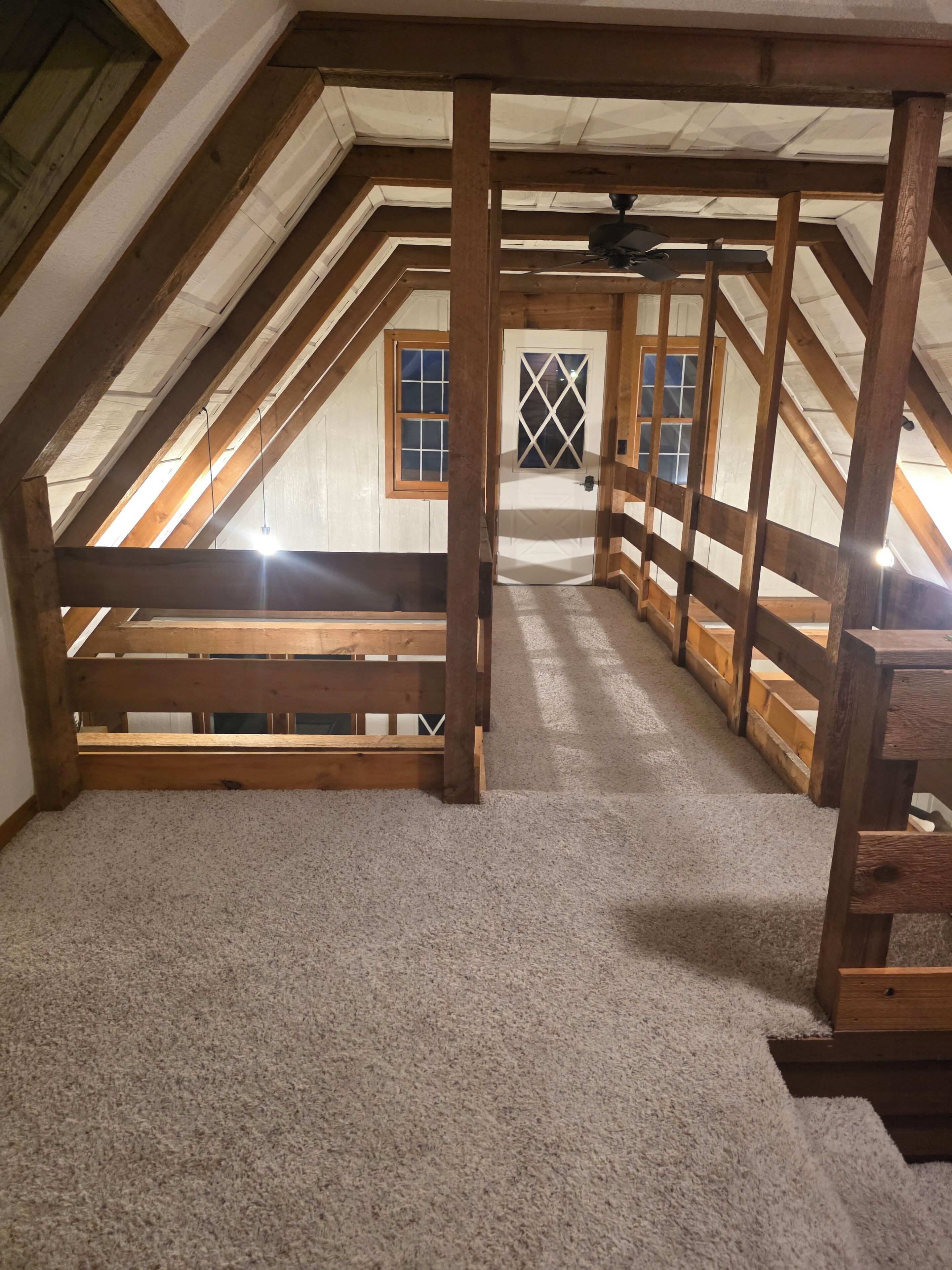 An attic room with wooden beams, a sloped ceiling, and a carpeted floor.