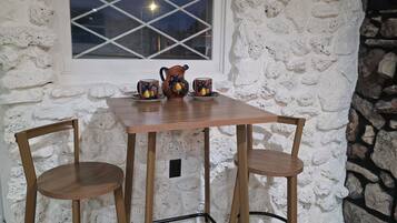 A stone-walled room with a table and two chairs, a window with a view of the night sky, and a decorative pitcher.