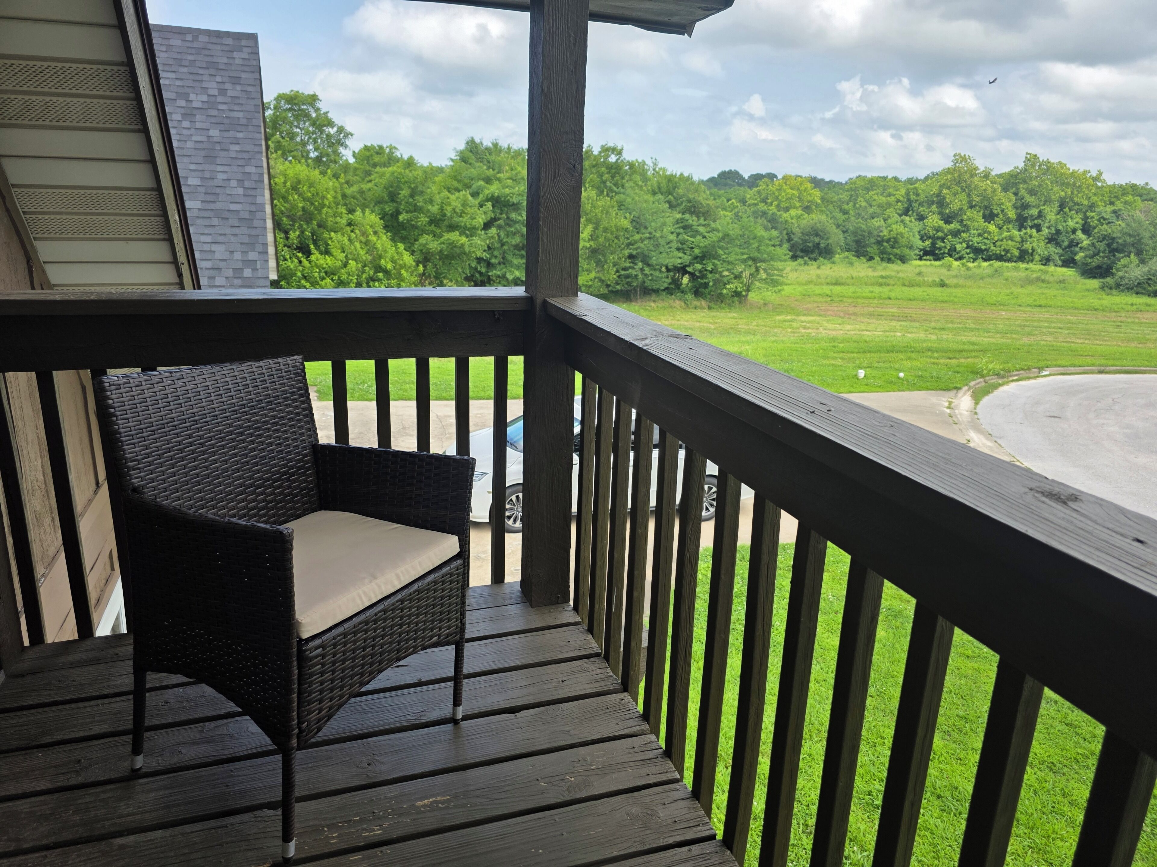 A wooden deck with a wicker chair, overlooking a grassy area and a body of water.