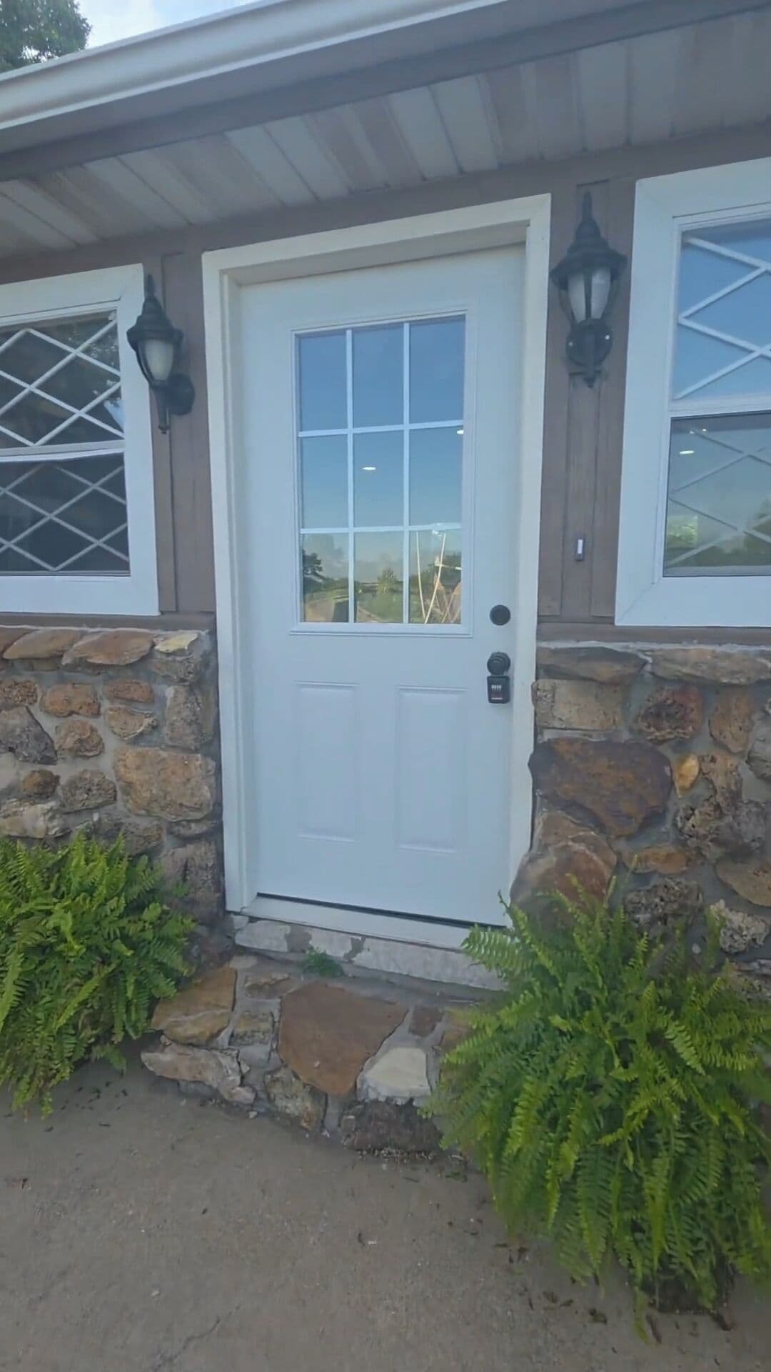 A white door with a glass panel, flanked by stone walls and two lantern-style lights.