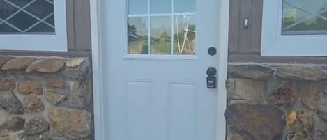 A white door with a glass panel, flanked by stone walls and two lantern-style lights.