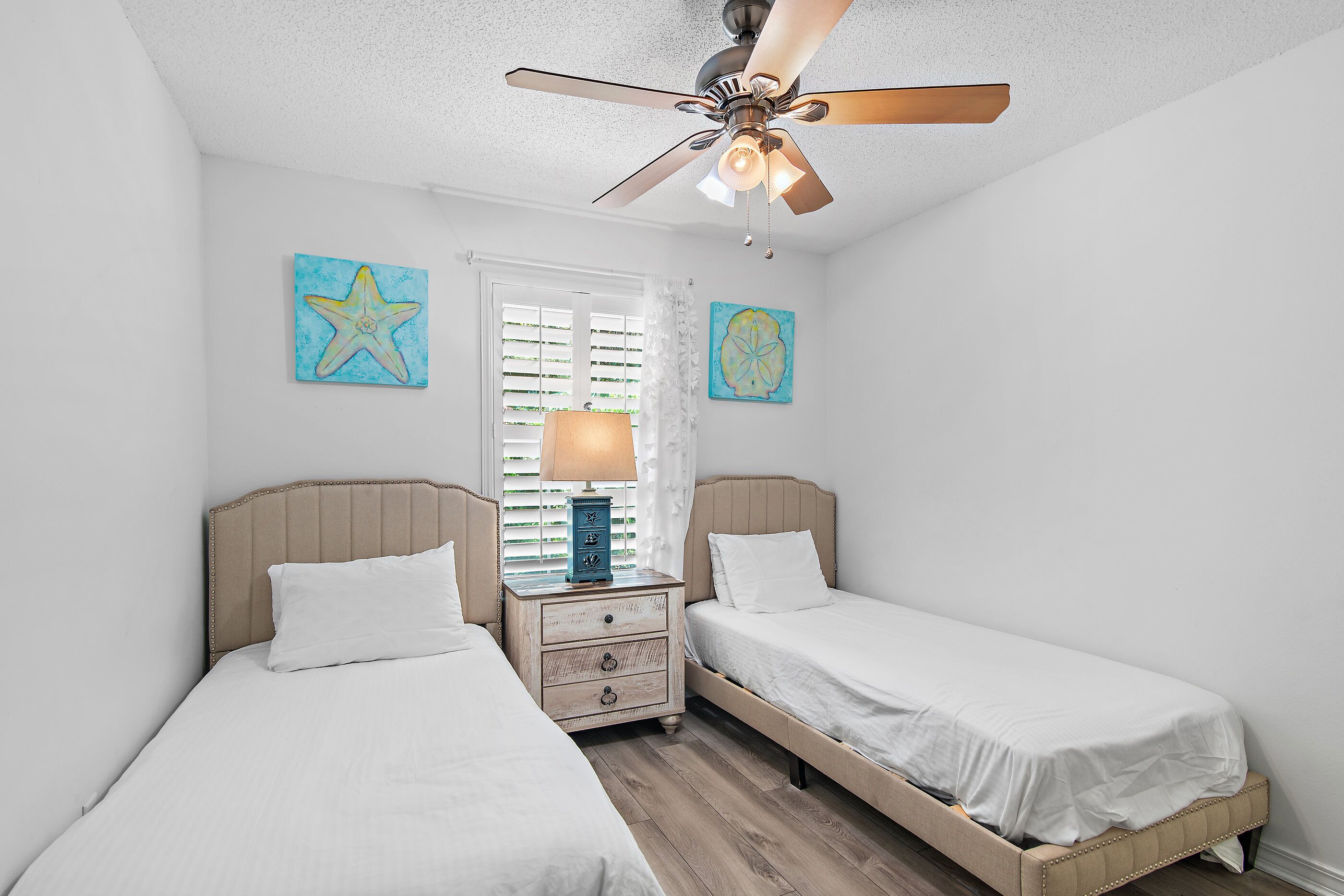 Une chambre avec deux lits, un ventilateur de plafond et des œuvres d’art accrochées aux murs.