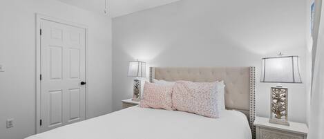 A bedroom with a bed, nightstands, lamps, a ceiling fan, and a door.