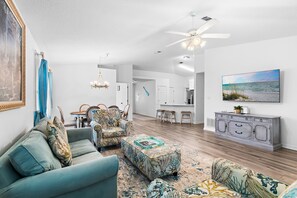 A spacious living room with a sofa, ottoman, and chairs, a dining area with a table and chairs, a kitchen with a white cabinet, and a ceiling fan. - ☀️Saltwater Haven | 0.2 Miles to Beach, Pool Access & Pets Welcome☀️ (Miramar Beach)
