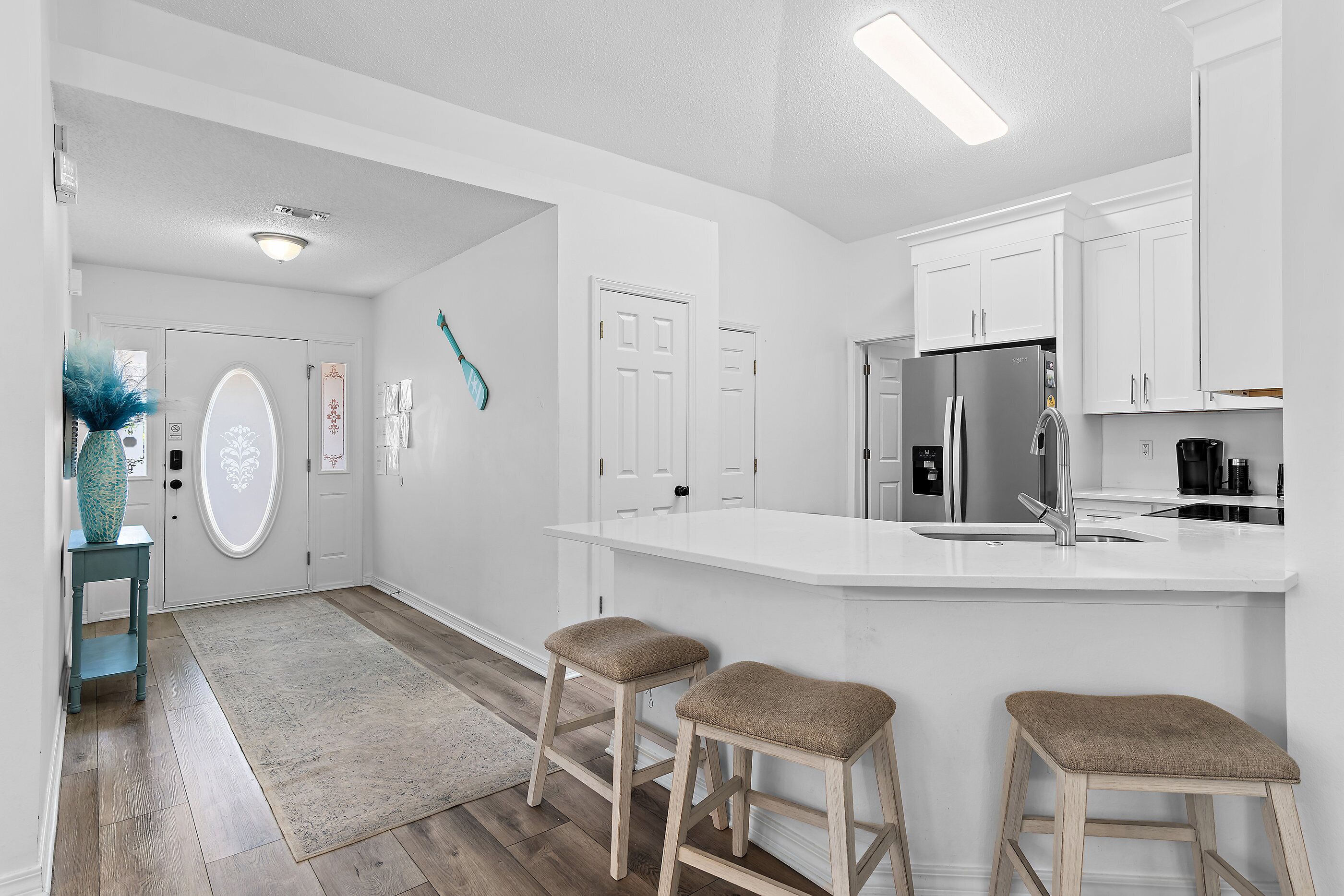 A modern kitchen with white cabinetry, a stainless steel refrigerator, and a bar stool area.