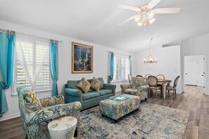 A living room with a sofa, ottoman, chairs, a dining table, and a ceiling fan. - ☀️Saltwater Haven | 0.2 Miles to Beach, Pool Access & Pets Welcome☀️ (Miramar Beach)